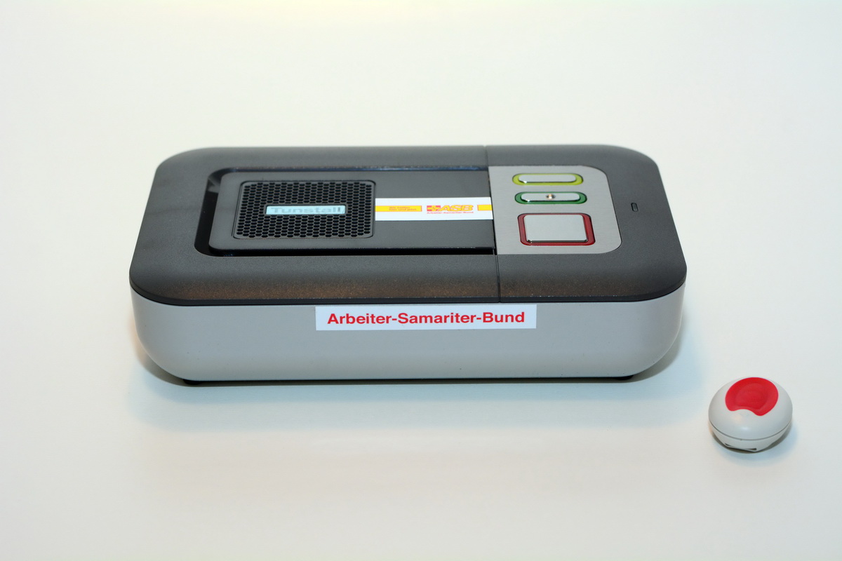 Das Hausnotrufgerät PiperFon Lifeline Vi besteht aus einem grauen Kasten mit nur drei Tasten und einem kleinen Sender,der etwas größer als eine 2-Euro-Münze ist